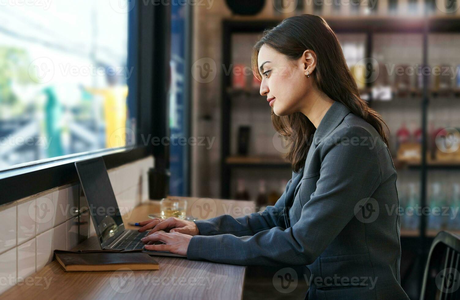 attractive business woman in suit sitting at counter bar, young modern female remote work, a digital nomad working over laptop internet online in cafe indoors photo