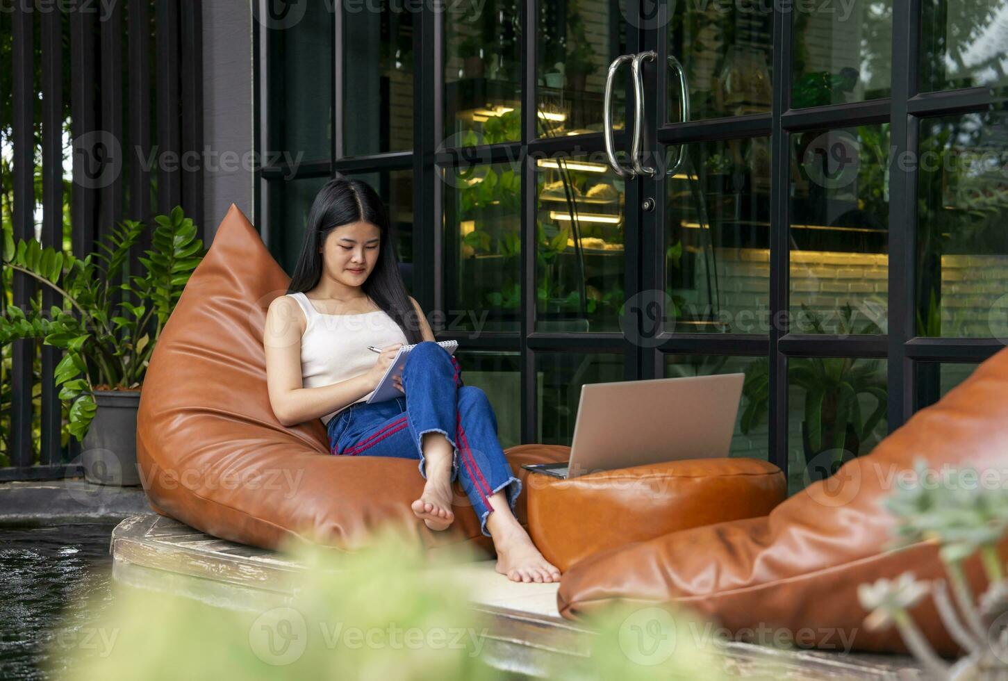 joven atractivo asiático mujer tomando Nota y trabajando terminado ordenador portátil en descansando zona a el hotel durante viaje en vacaciones, concepto de digital nómada,viajar libremente, trabajando remotamente en Internet en línea foto