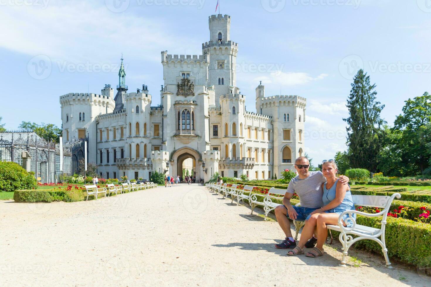 A couple of tourists are sitting on a bench in front of the beautiful castle Hluboka nad Vltavou - Czech Republic. photo