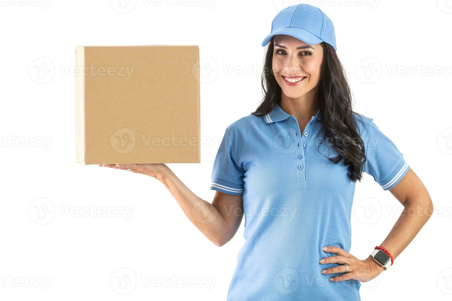 Dark-haired smiling courier in blue cap and t-shirt uniform happily holding a cardboard parcel ready to deliver. Isolated background photo