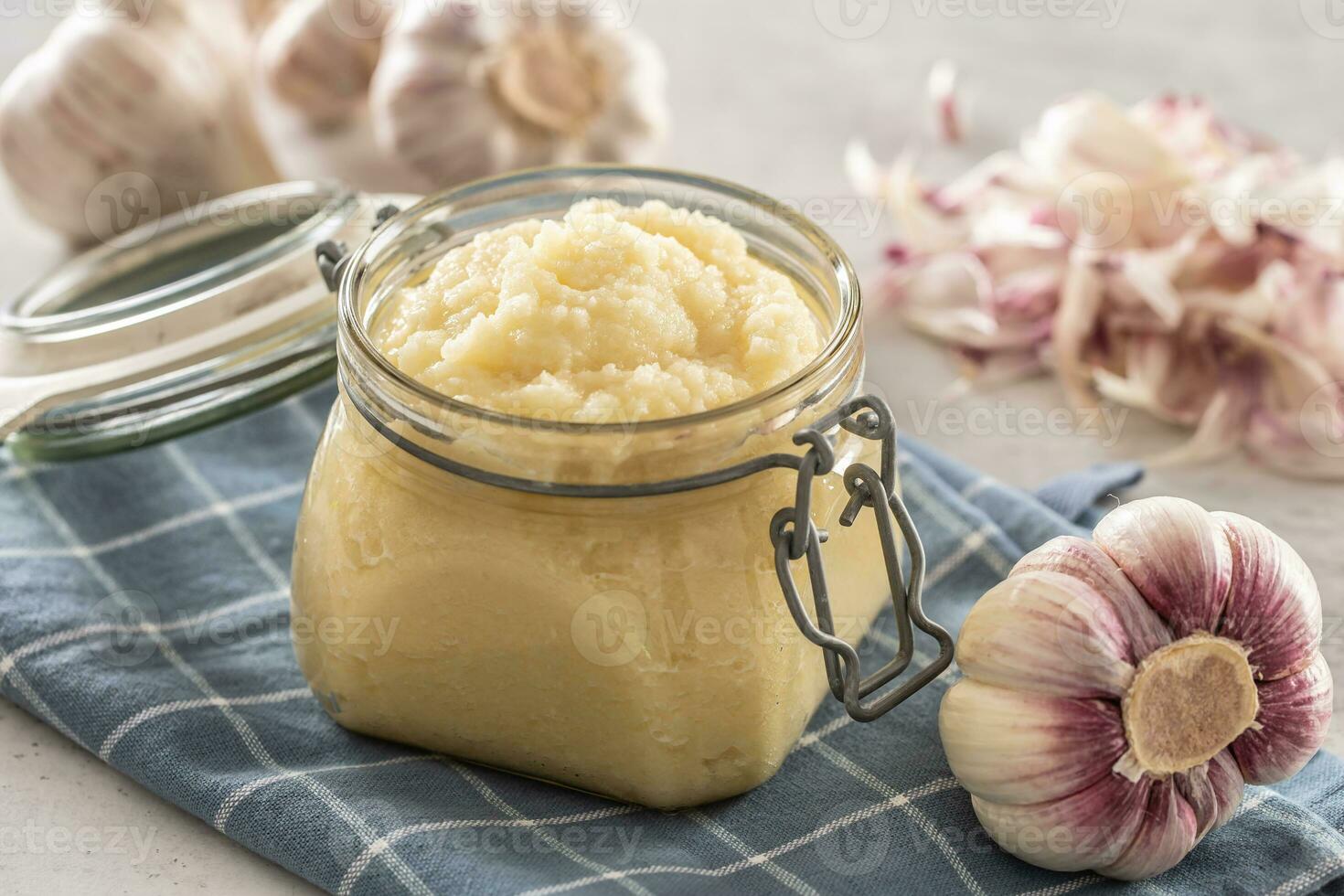 Aromatic garlic paste in a glass jar laid on rustic kitchen cloth with bulbs and peeled cloves photo