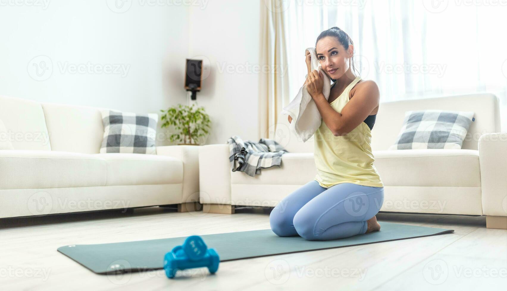 Home workout finish by a good looking girl wiping sweat of her forehead kneeing inside the house photo
