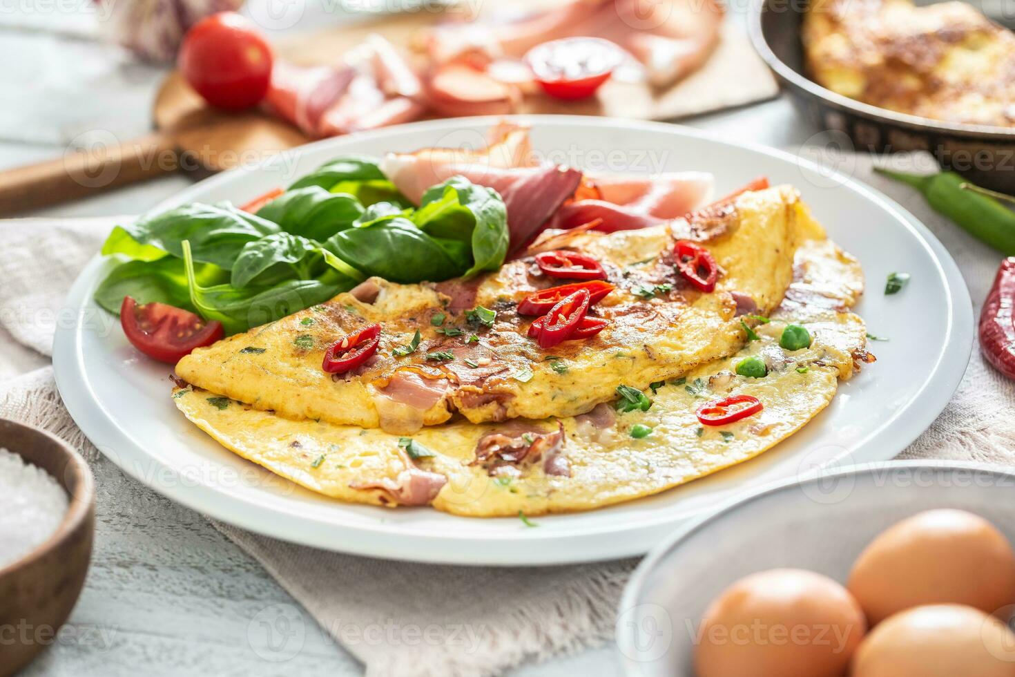 Omelette with prosciutto peas basil tomatoes and herbs on white plate photo