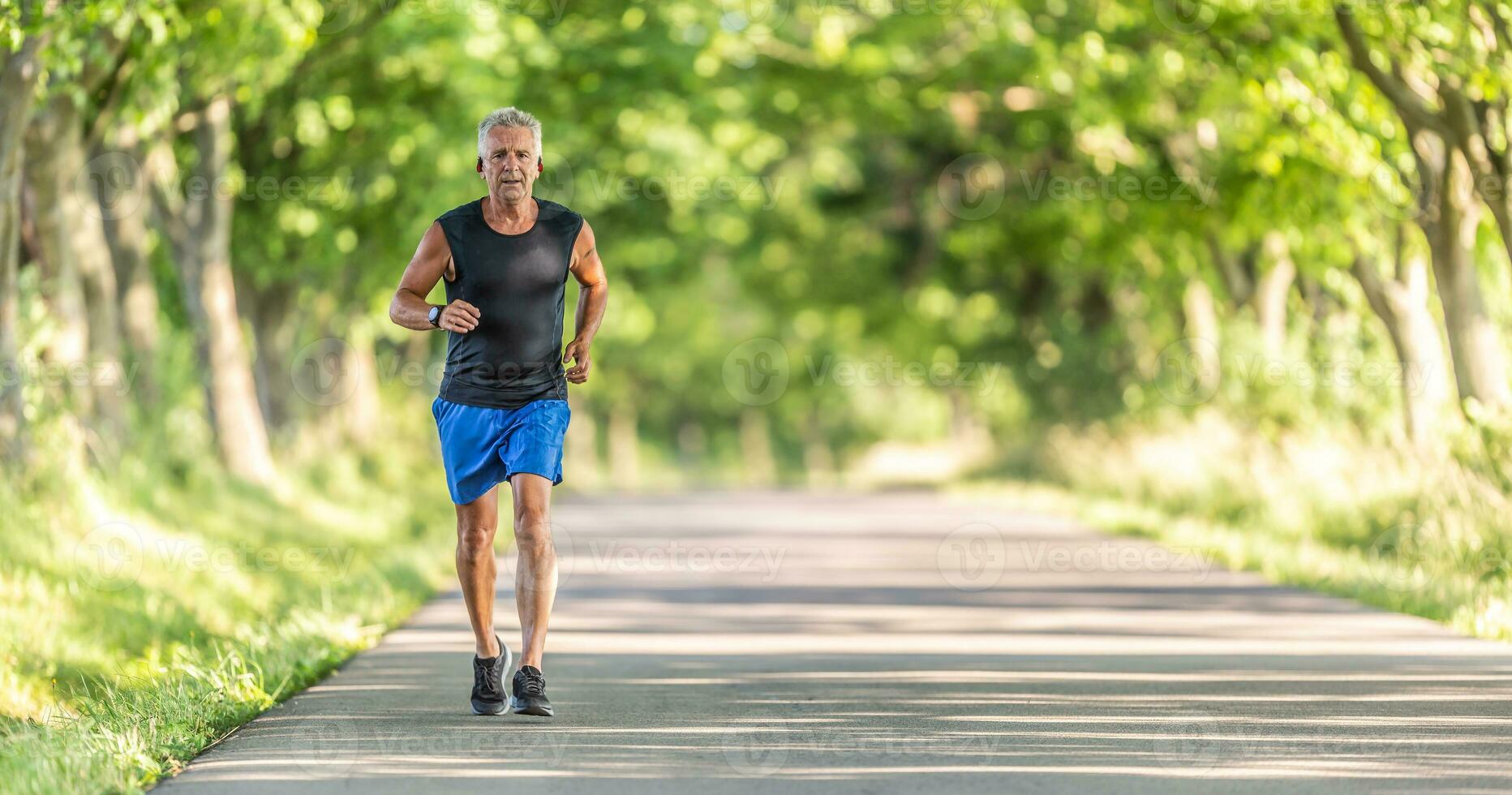 Older man runs uphill in the nature during a summer day keeping his fitness level high photo