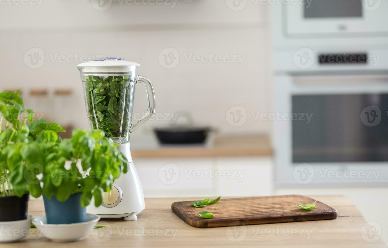 Kitchen with fresh herbs, green leaves inside the bledner and a chopping board photo