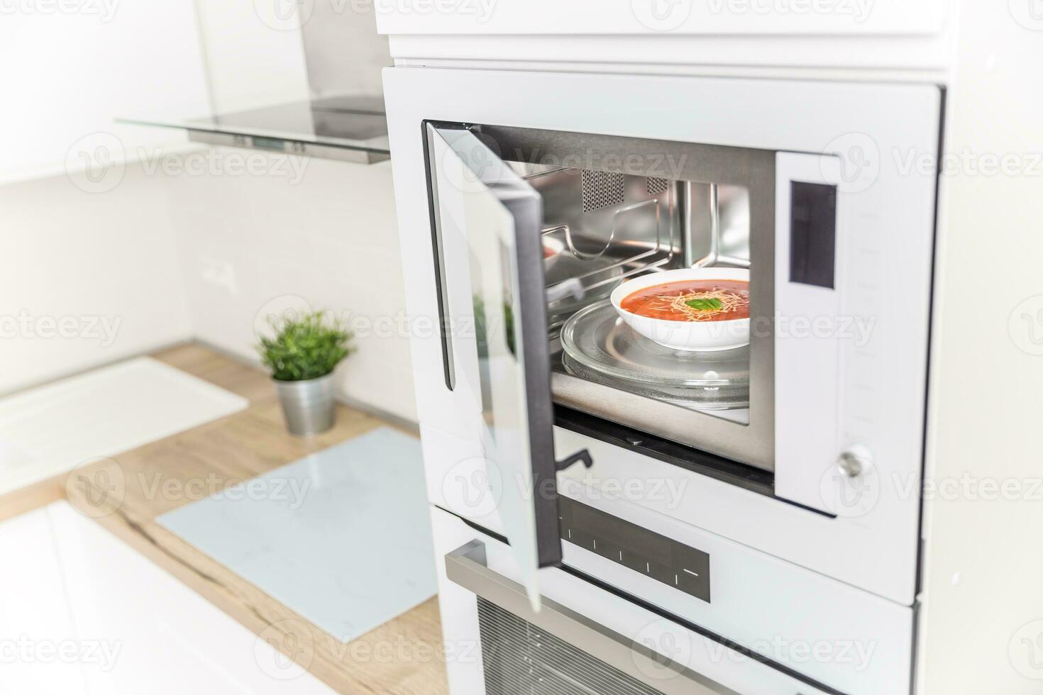 Built-in microwave oven  in the kitchen with tomato soup in white plate photo