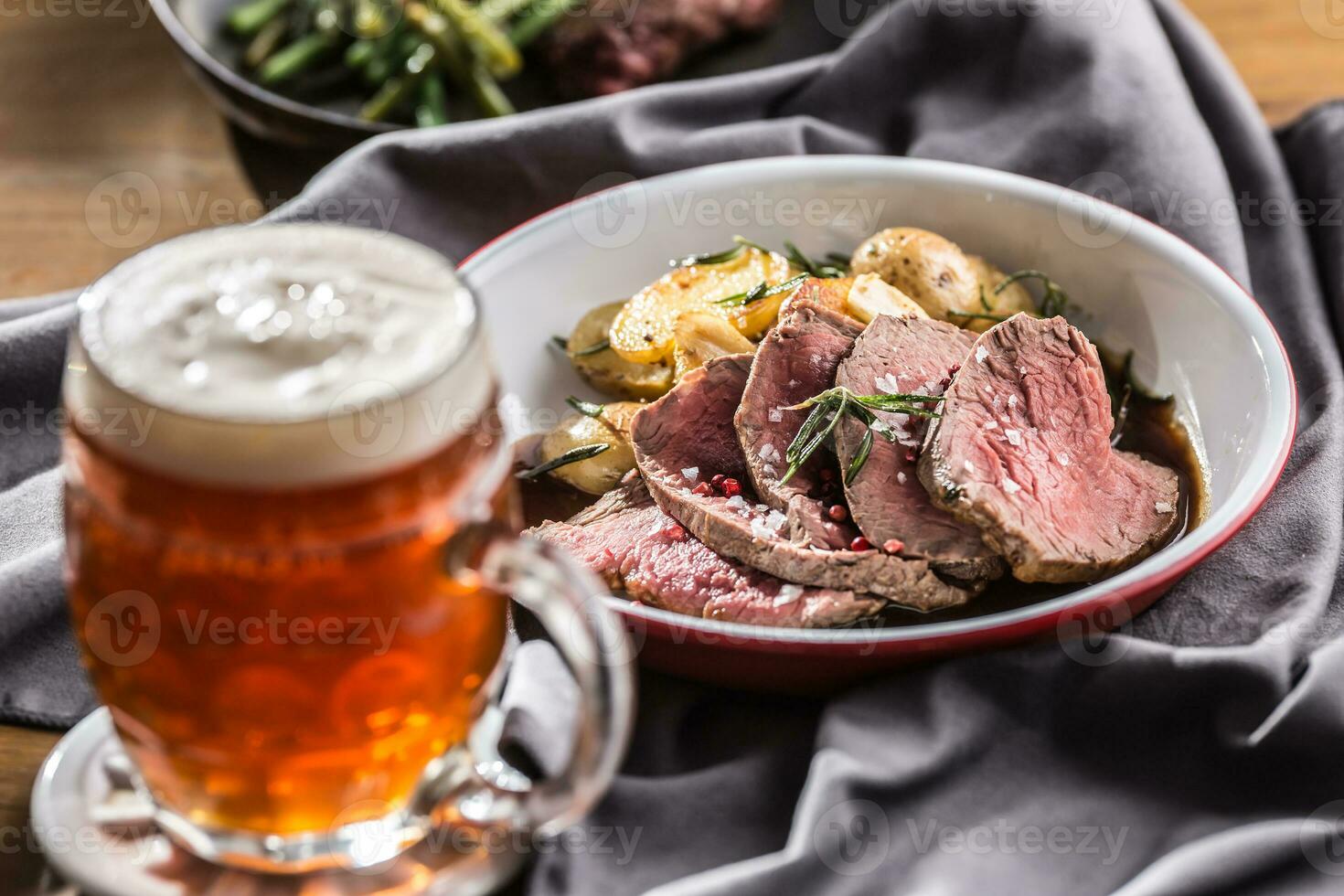 Sliced Beef tenderloin roasted steak potatoes rosemary and draft beer photo