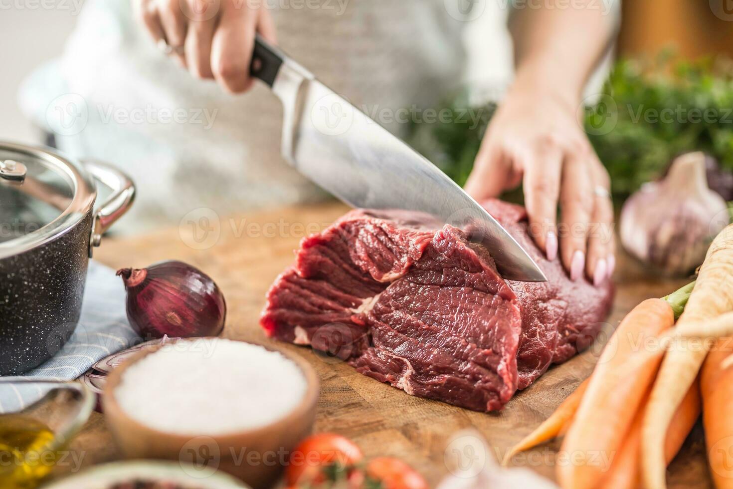 joven ama de casa rebanar Fresco carne de vaca filete. hembra manos preparando almuerzo de carne y vegetales foto