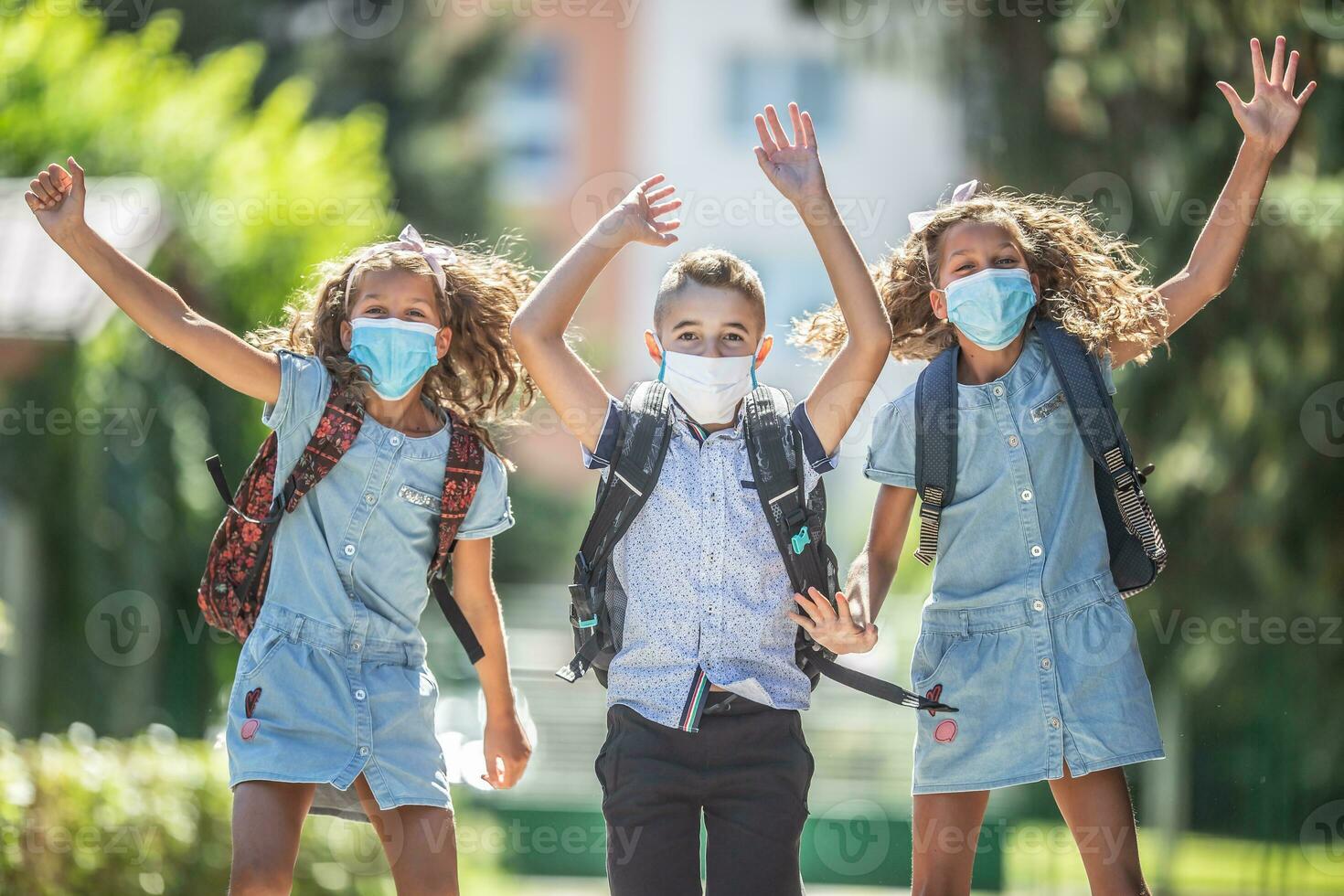 Happy schoolchildren with face masks jump from joy to return to school during the Covid-19 quarantine. photo