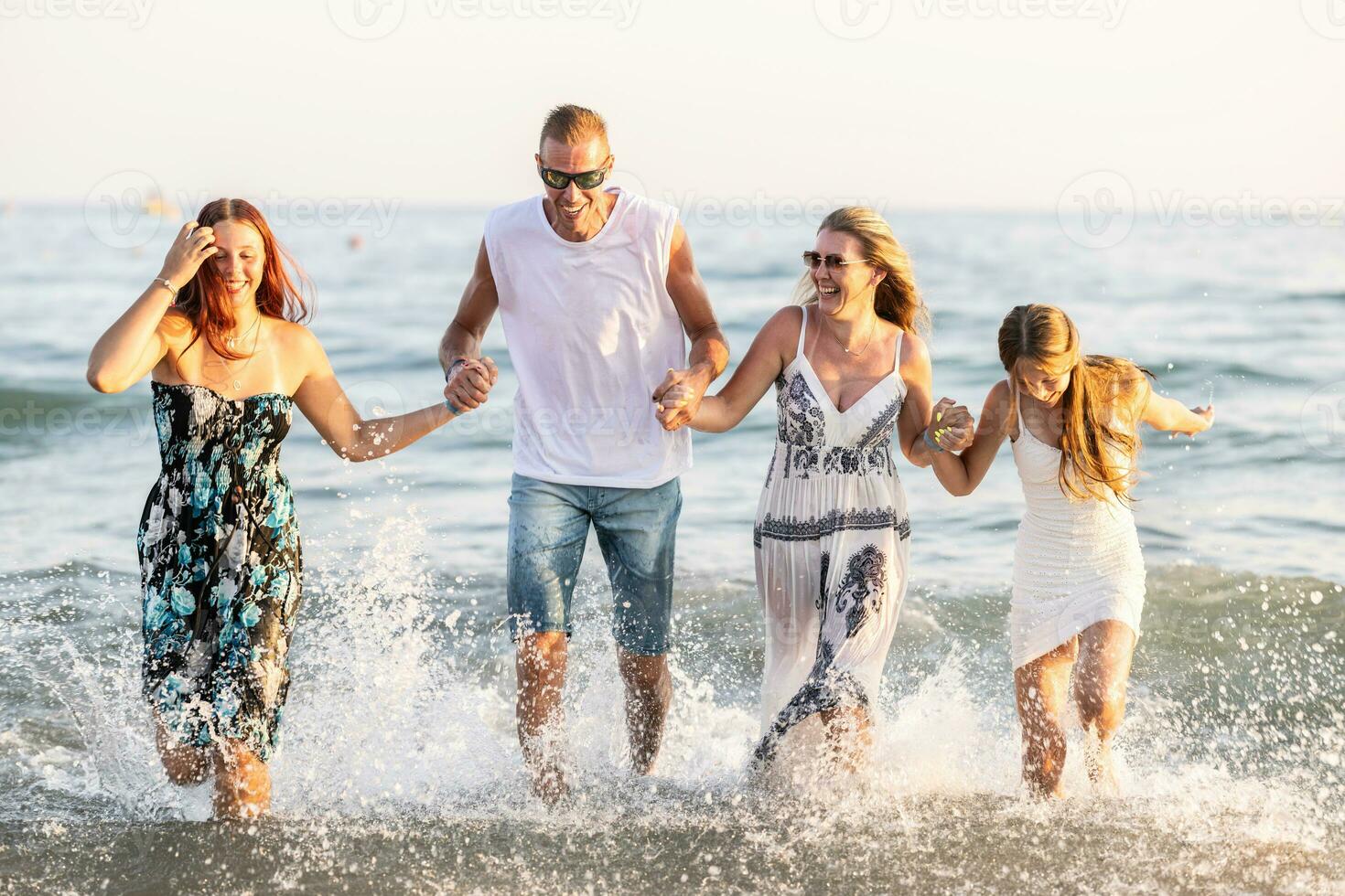 The complete family runs hand in hand from the beach to the sea, enjoying a joint vacation by the sea photo