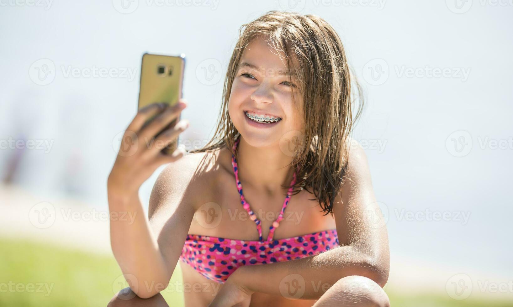 Happy young girl with dental braces making selfhie on beach in summer hot day photo