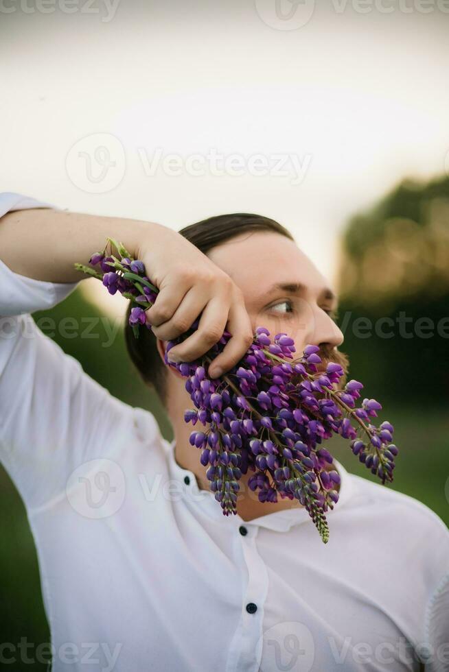 Young man with bouquet of lupines like a beard. Sunset or sunrise, bright evening light photo