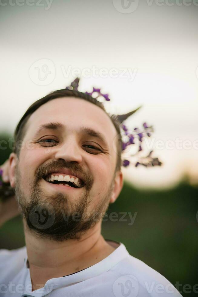 joven sonriente hombre con ramo de flores de altramuces me gusta un corona. puesta de sol o amanecer, brillante noche ligero foto