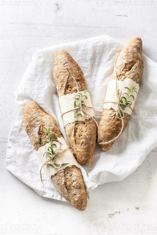 Top view of three baguettes or wholegrain breads on a linen textile white surface photo