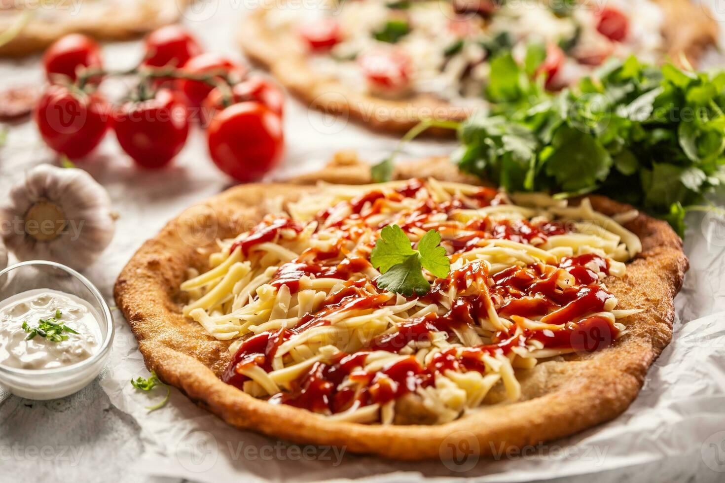 Cheesy hungarian traditionaly baked langos with ketchup, garlic and herbs served on a baking paper with tomatoes and vegetables and sour cream photo