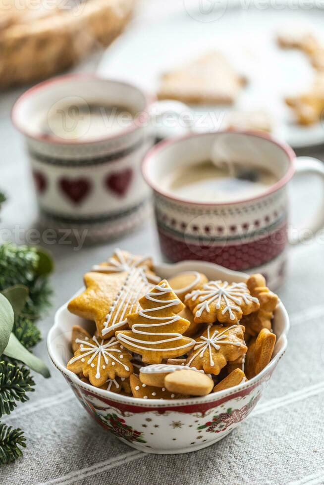 A bowl full of Christmas gingerbread on the table led an Advent wreath and two cups with coffee, punch or tea photo