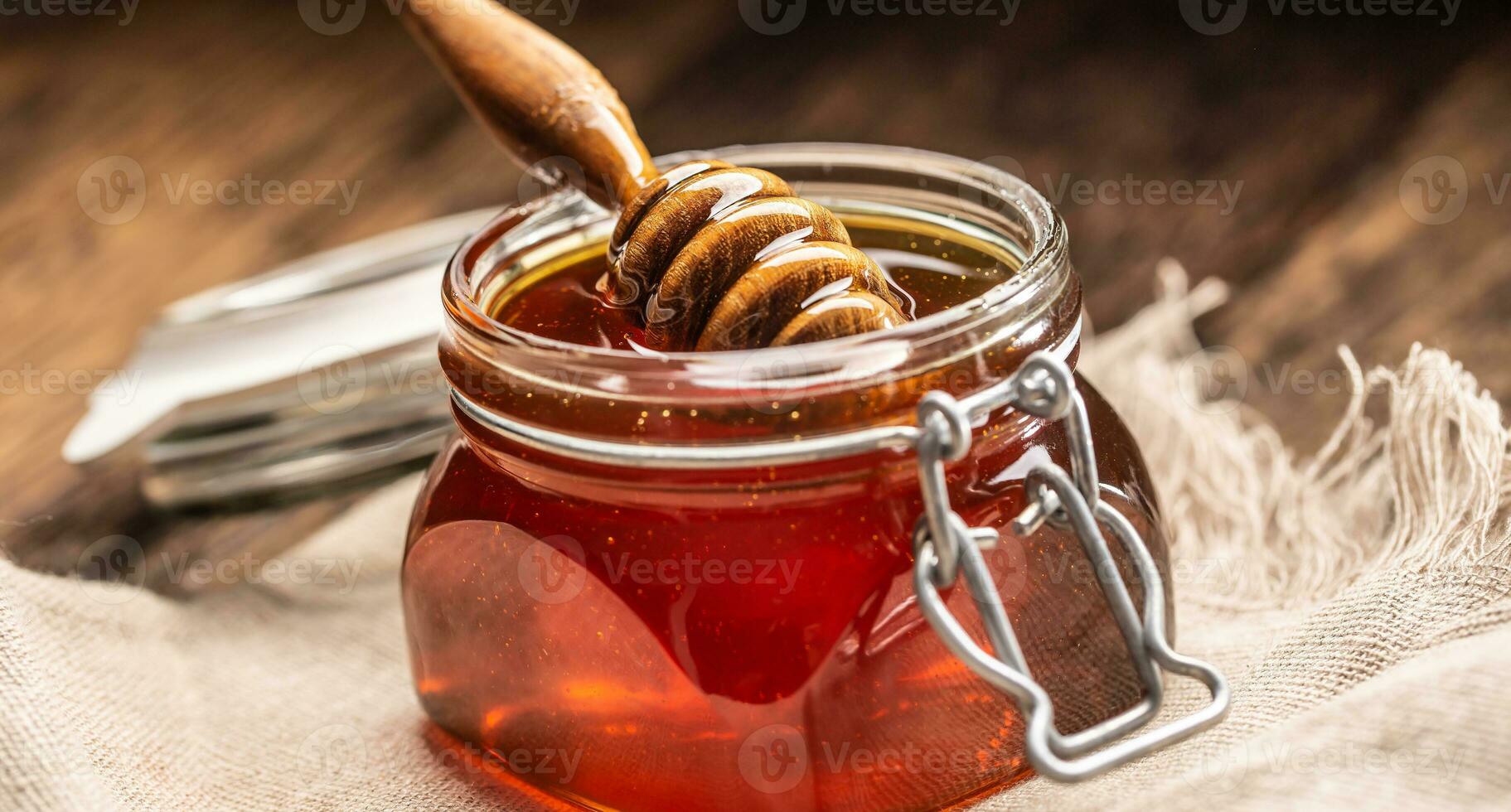 Jar of honey with dipper on wooden table - closeup photo