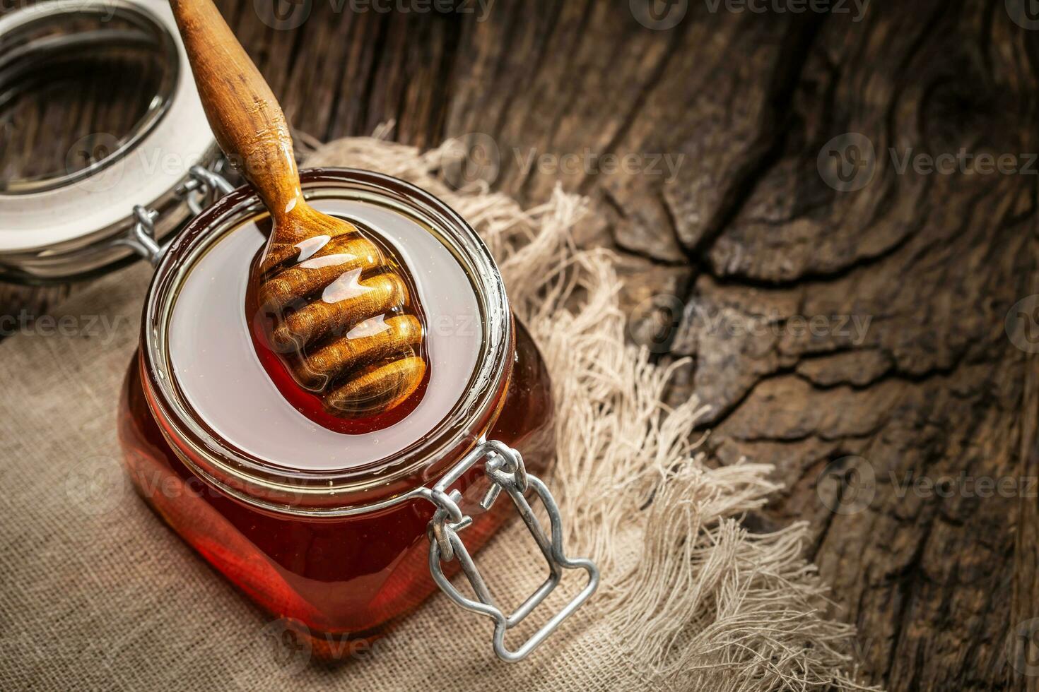 Jar of honey with dipper on wooden table - closeup photo