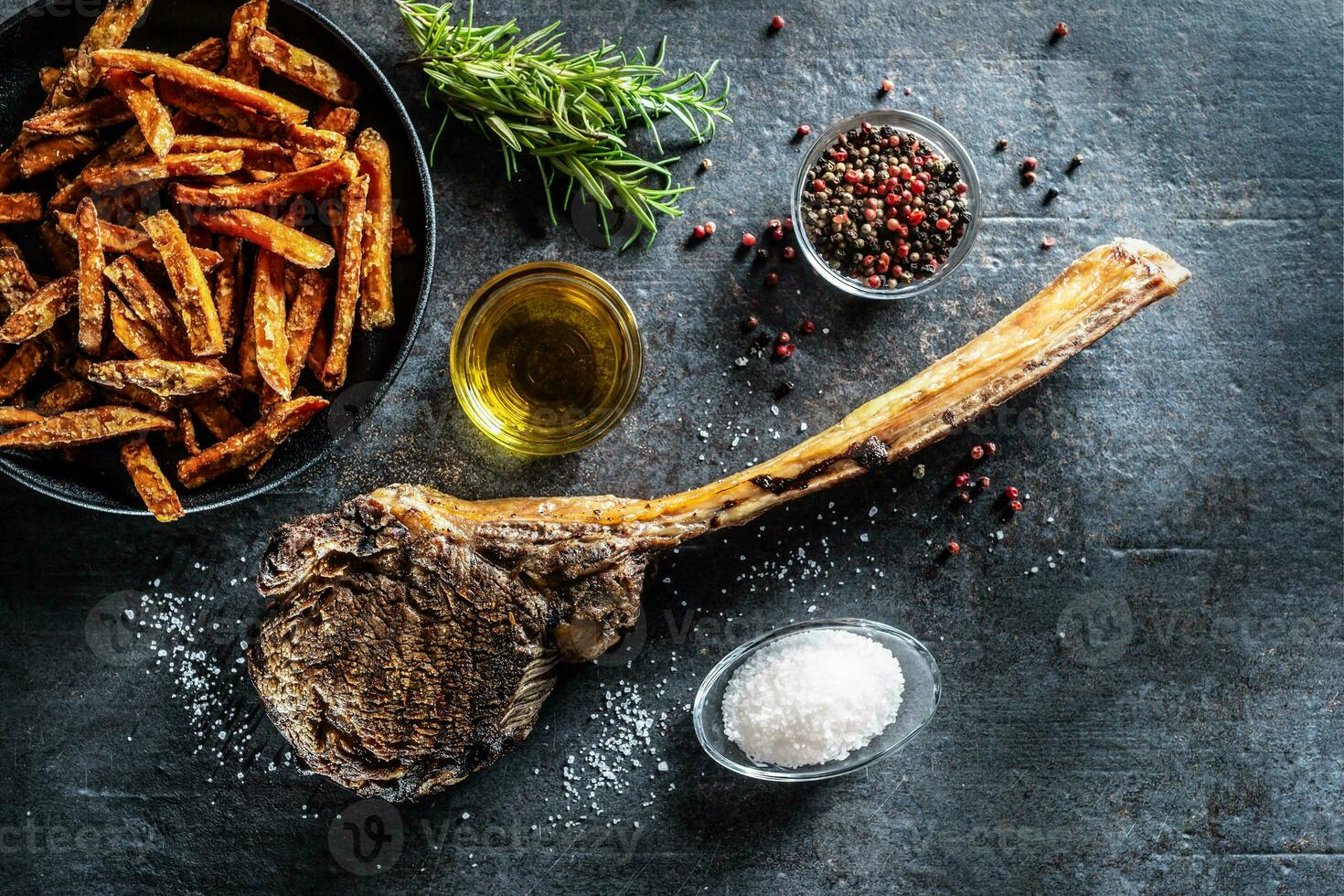 Grilled beef tomahawk steak with sweet potato fries salt spices olive oil and rosemary on rustic board - top of view photo