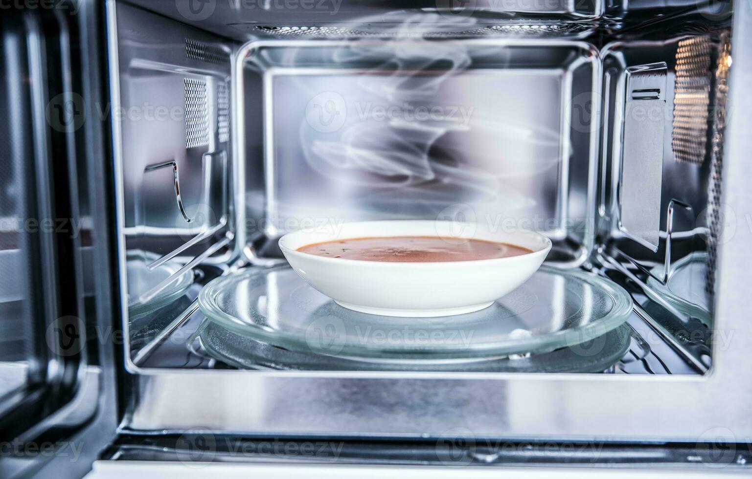 Inside view of new clean staniless microwave oven with a tomato soup in white plate photo