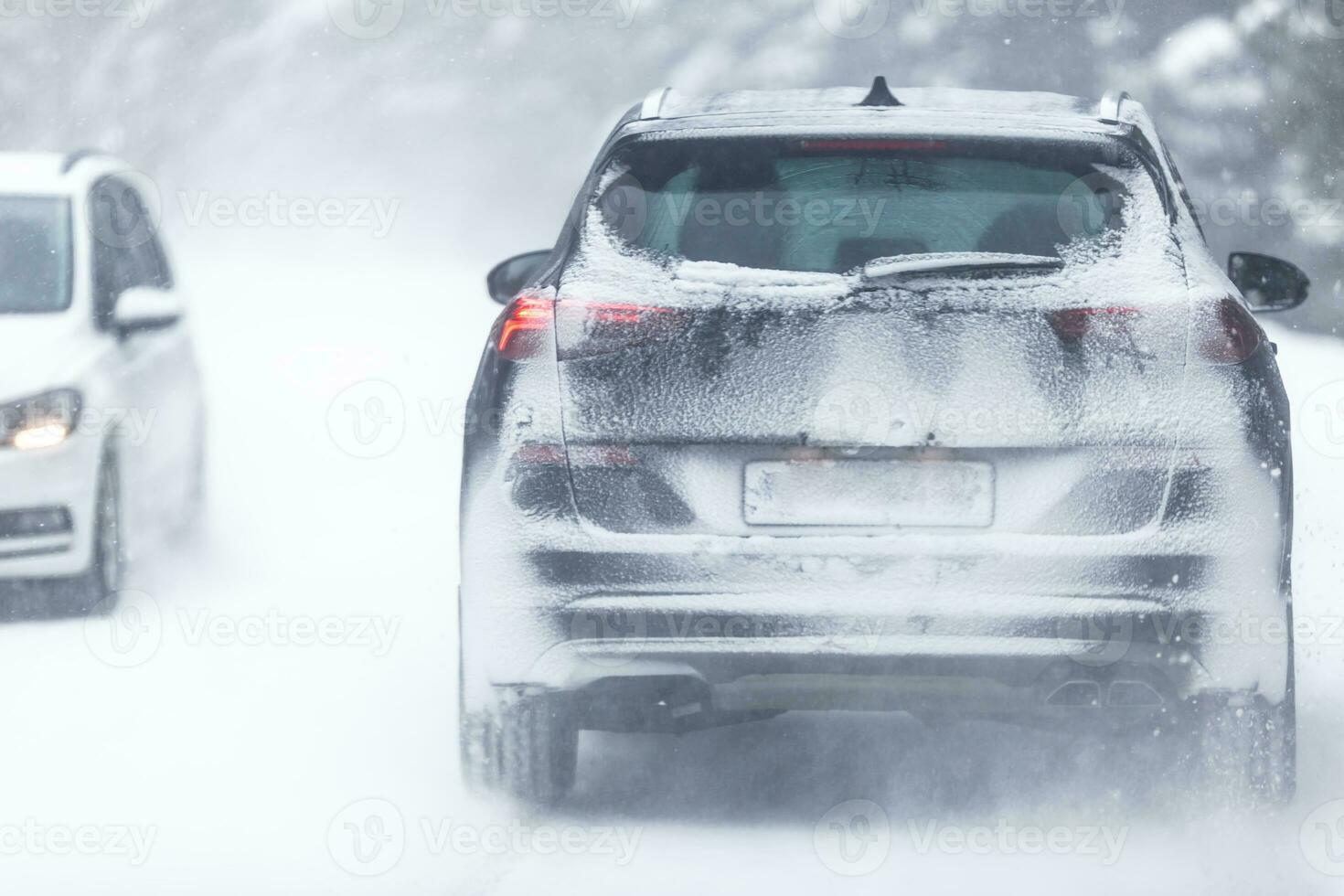 SUV car driving on snowy slippery road inside the forest, having registration number insivisible due to snow photo