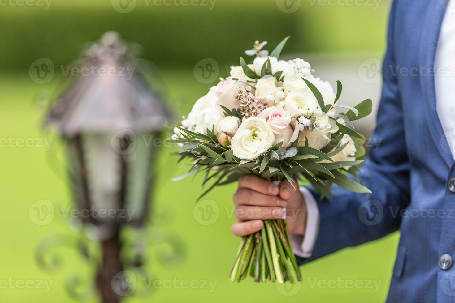 Groom holds a wedding bouquet with white flowers outdoors on a wedding day photo