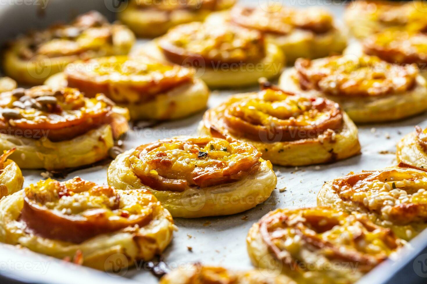 Rolls of puff pastry with ham bacon cheese sesame on baking tray photo