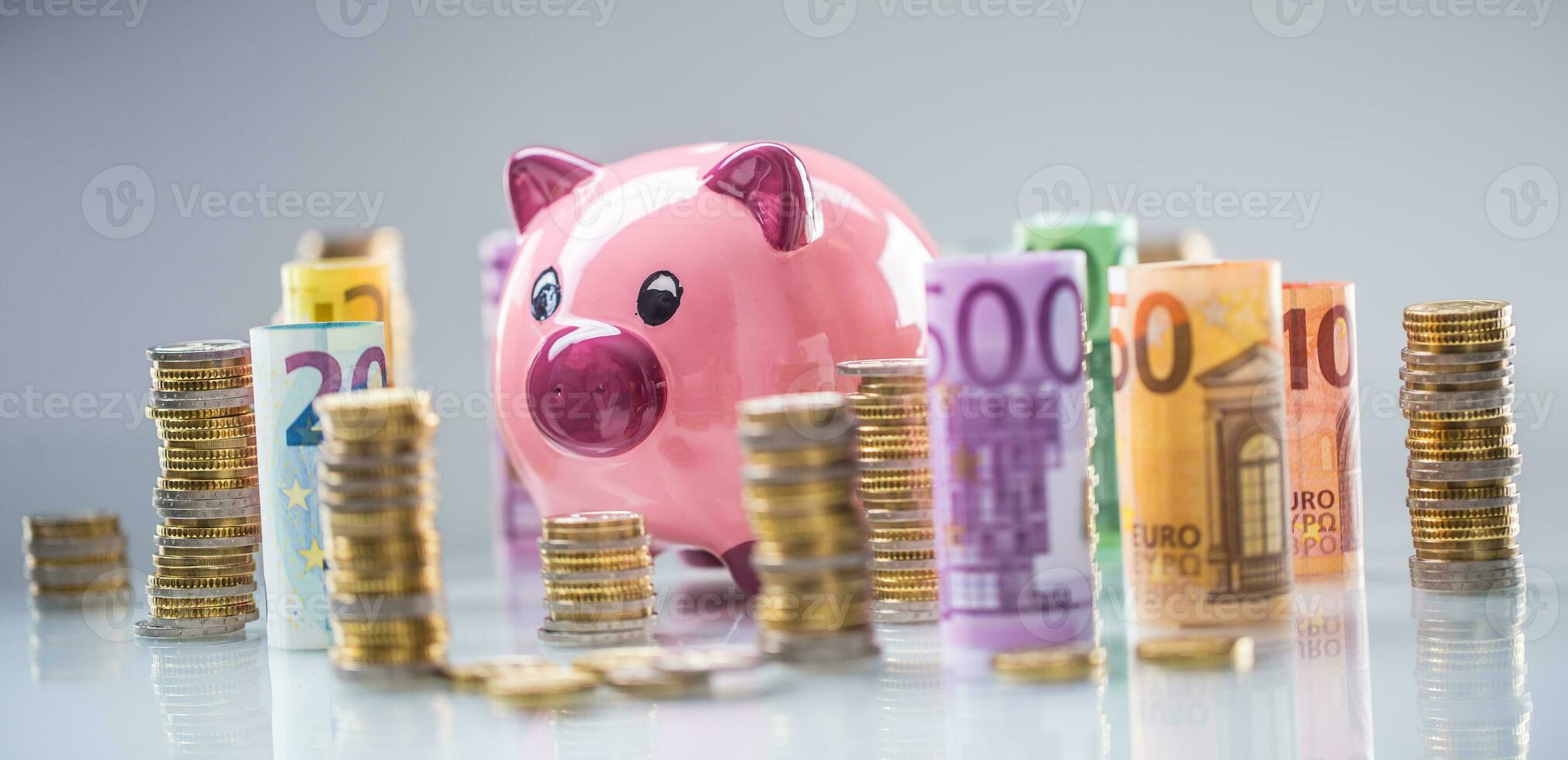 Pink piggy bank in the middle of rolled euro banknotes and towers with coins photo