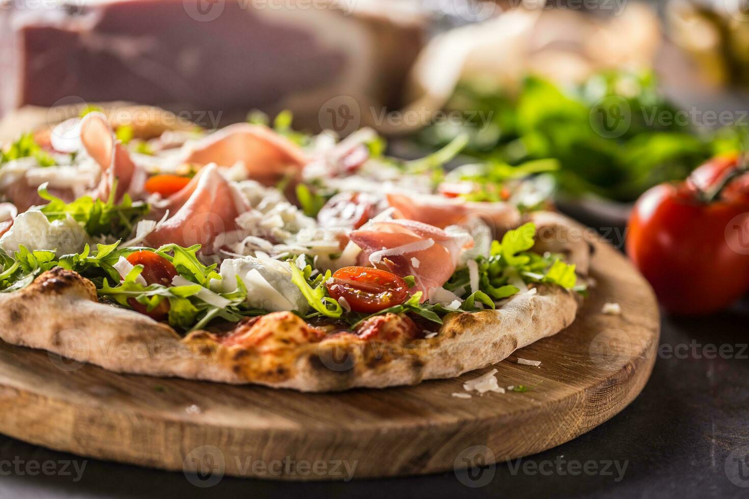 Italian pizza with prosciutto arugula tomatoes and parmesan on wooden round board photo