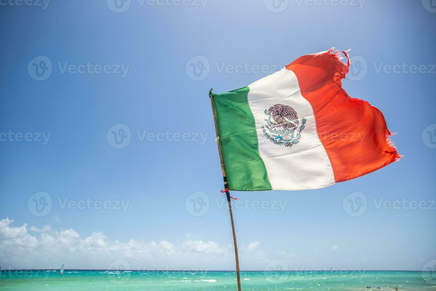 Mexican flag partially ripped by the wind blowing from the turquiose Carribean Sea photo