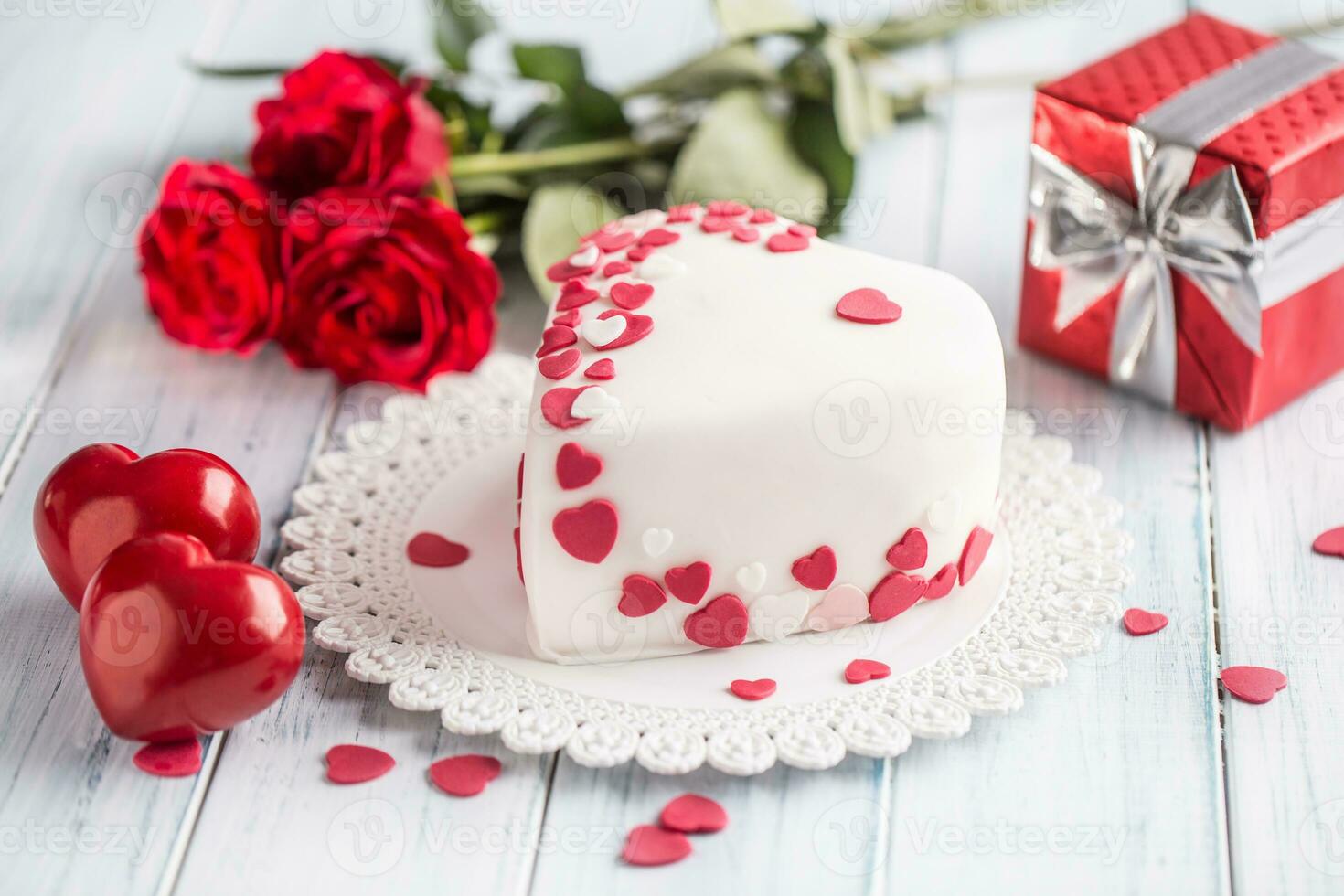 Marzipan white cake in the shape of a heart with red hearts. As the decoration bouquet of red roses a gift from the ribbon. Wedding or valentines day concept. photo