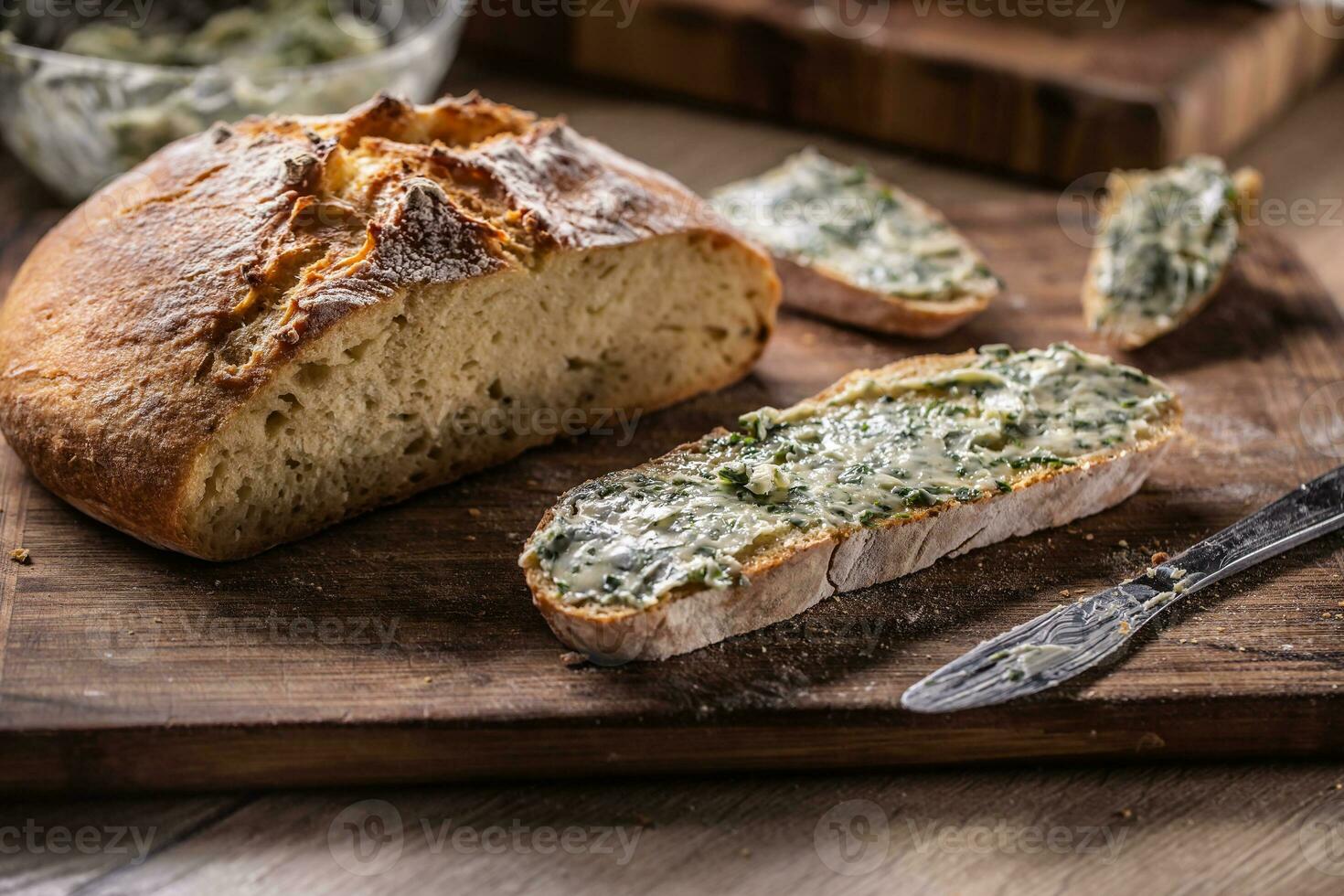 Slice of bread with herb butter next to a freshly baked crusty bread loaf next to it photo