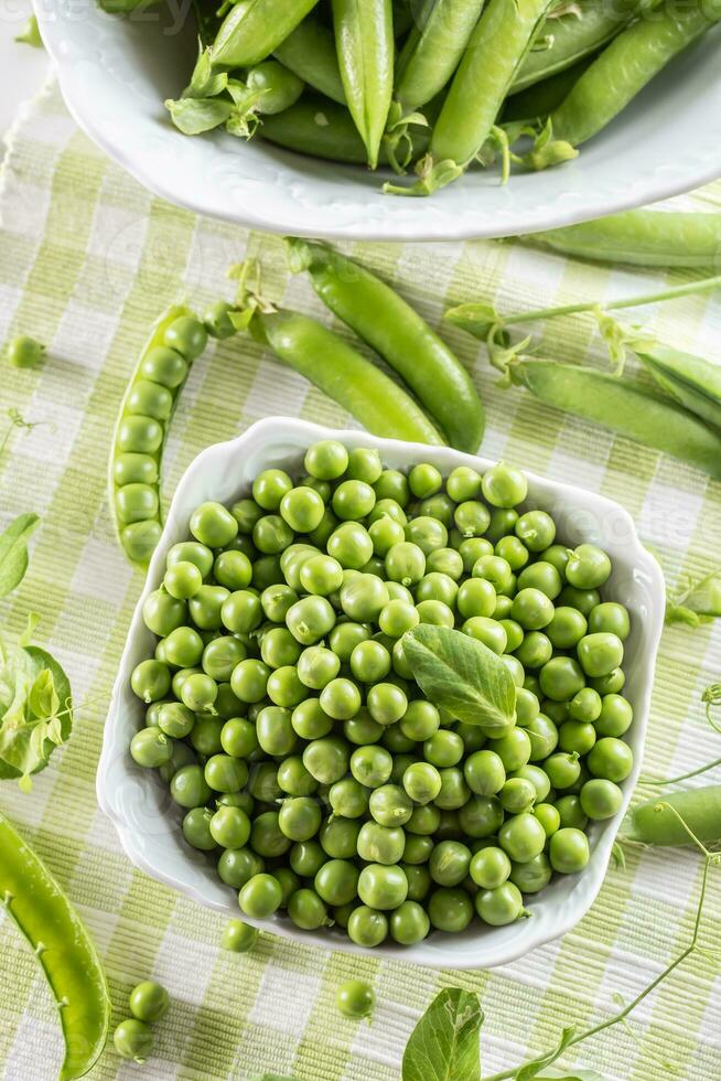 Green raw peas and pods in pocelain bow isolated on wooden table photo