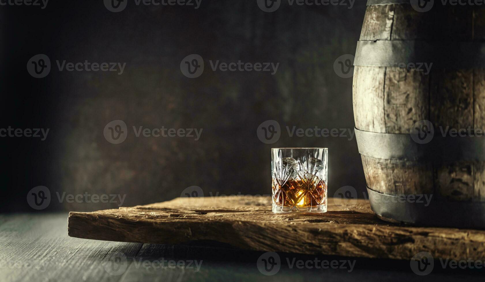 vaso de whisky o Borbón en ornamental vaso siguiente a un vinatge de madera barril en un rústico madera y oscuro antecedentes foto