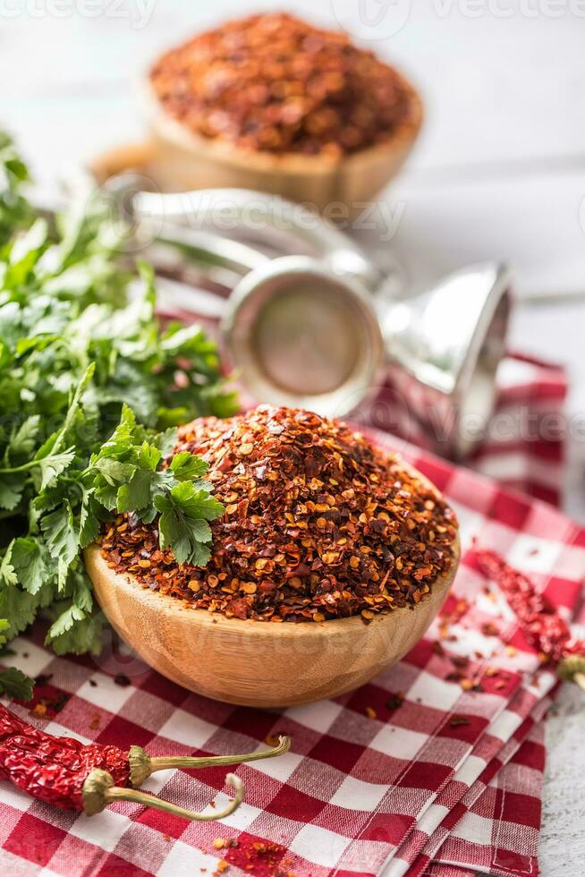 Dried and crushed chili peppers in wooden bowles with parsley herbs photo