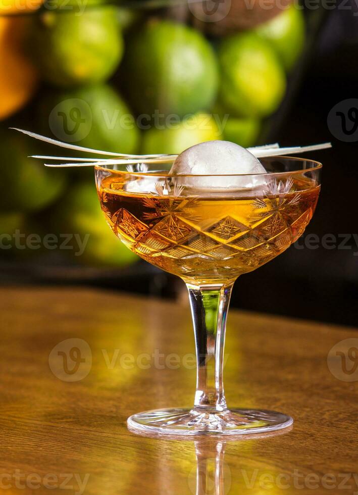 Tasty alcohol drink with large ice ball inside. Served in stylish glass with juicy limes in the background photo