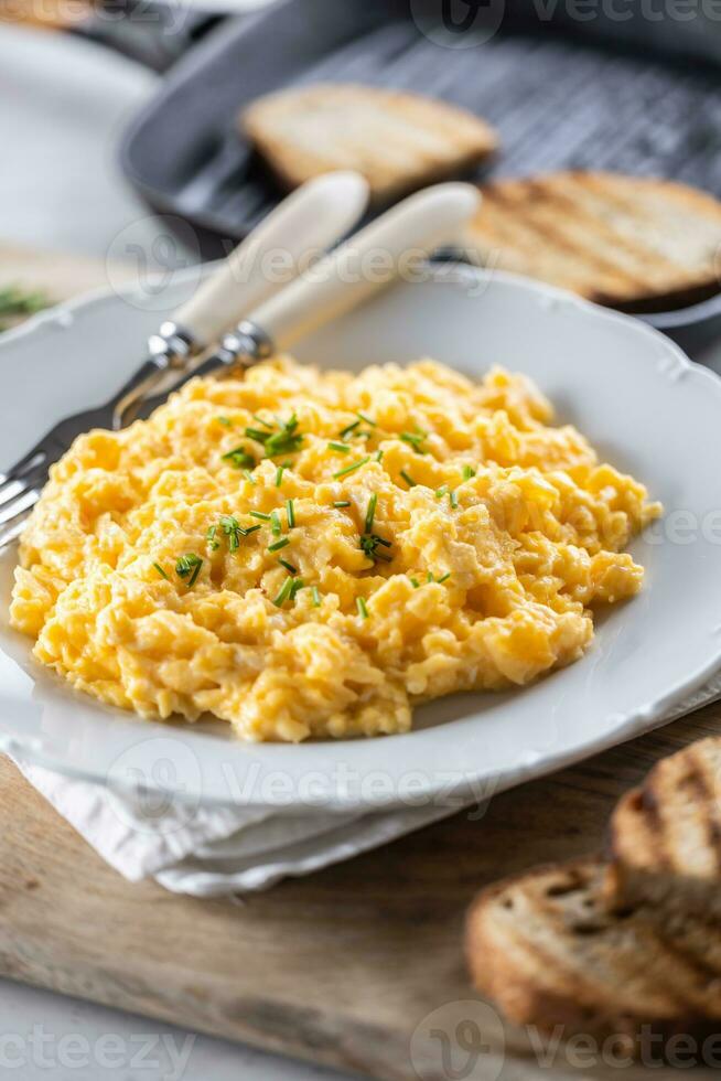 Tasty yellow freshly-made scrambled eggs with chives in a plate, served with toasted bread slices photo