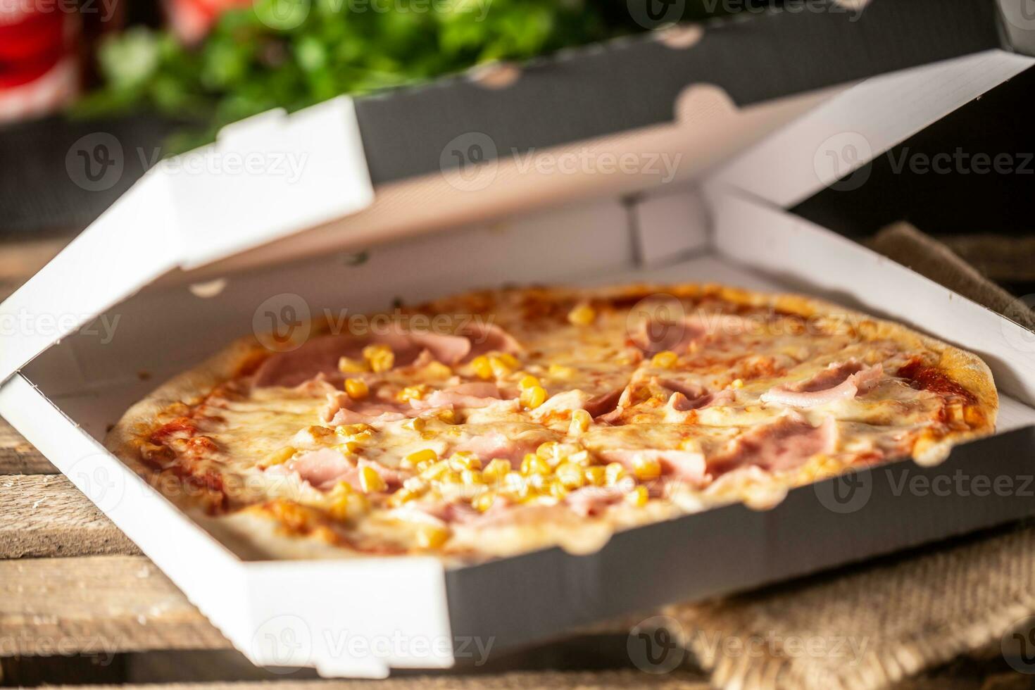 Pizza with ham, corn and cheese in a half-open white pizza box photo