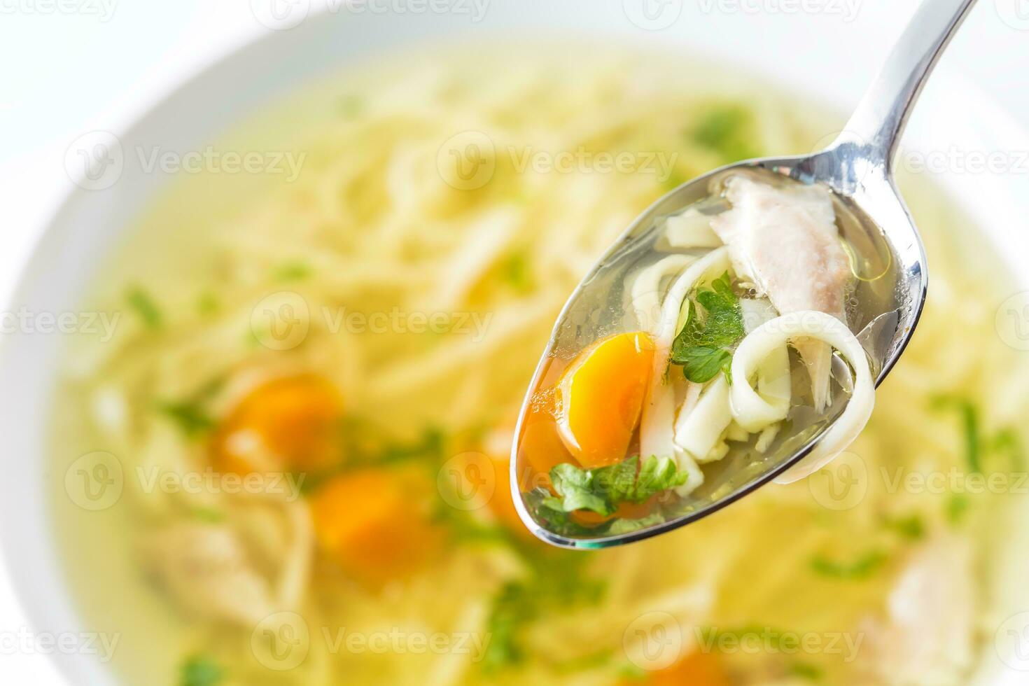 Spoon full of chicken or beef soup with noodles carrot and herbs photo