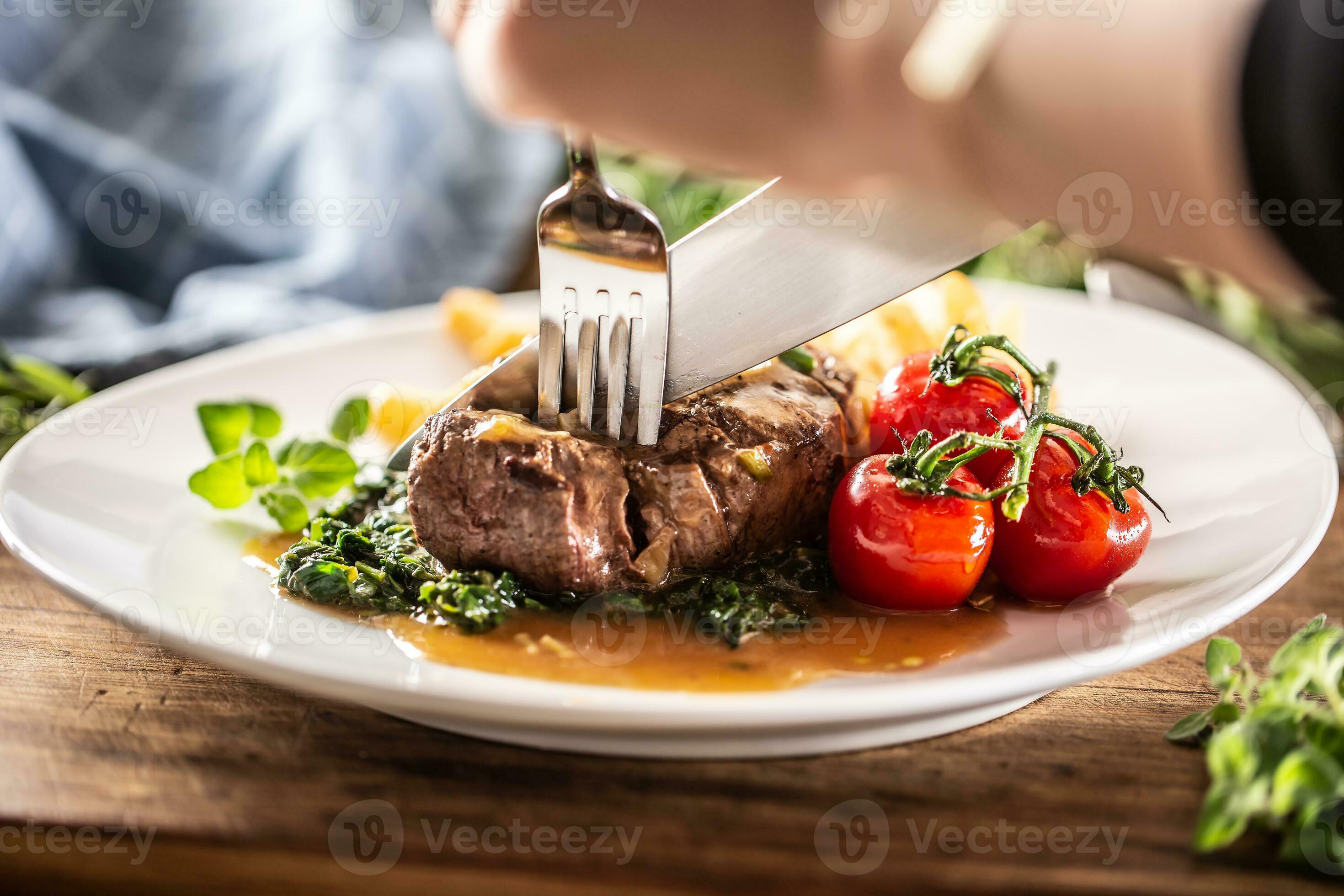 Person cuts into a cooked steak with fork and knife with vegetables on
