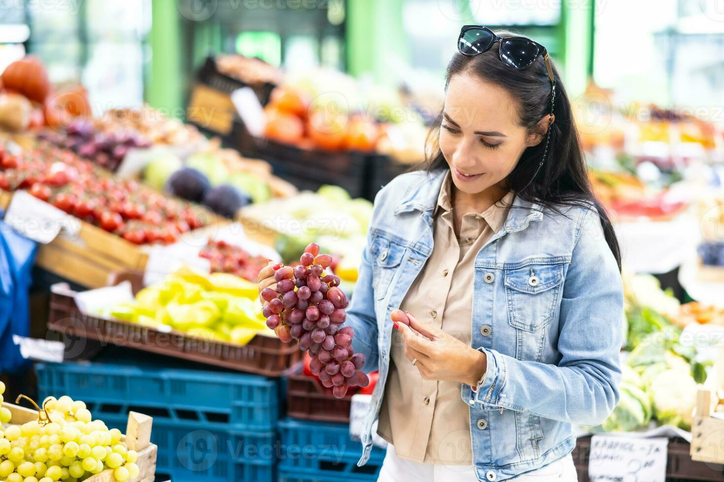 mujer escoge uno uva desde un manojo de rojo vino en su manos en el mercado foto