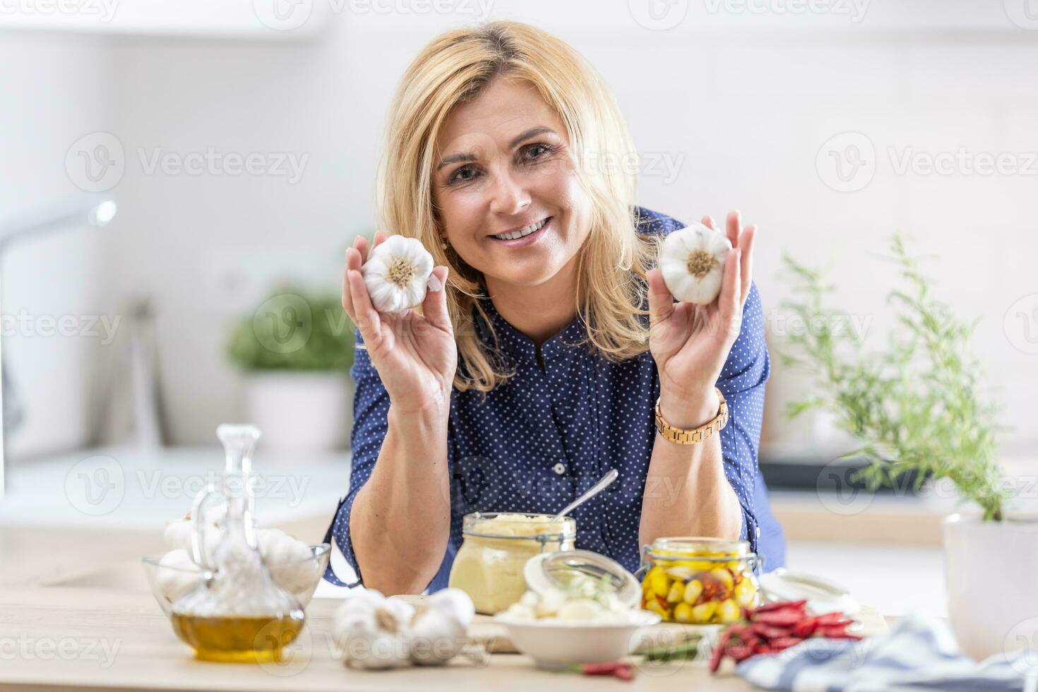 Woman holds garlic heads in her hands while various types of garlic preserves surround her photo