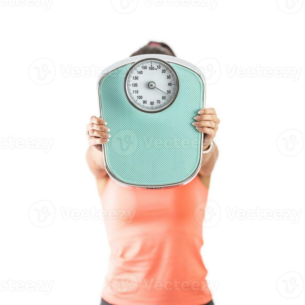 Woman holds a weighing scale against the camera covering her face with it photo