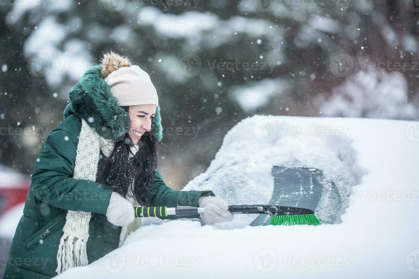 Woman struggles to scrape ice and snow off the snowed-in car on a parking lot photo