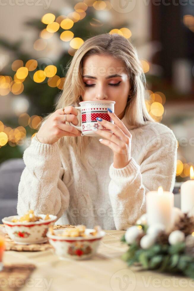 un hermosa joven rubia mujer sabores Navidad puñetazo, té reflexionado vino o café. foto