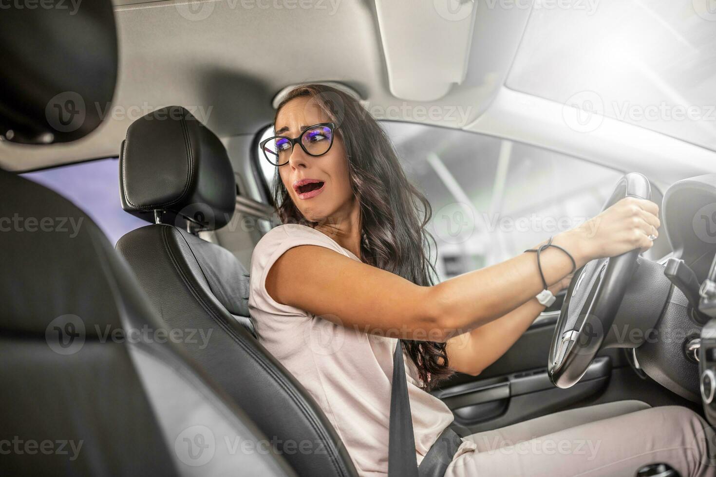 Unexperienced driver with frightened facial expression reverses car looking over her shoulder photo