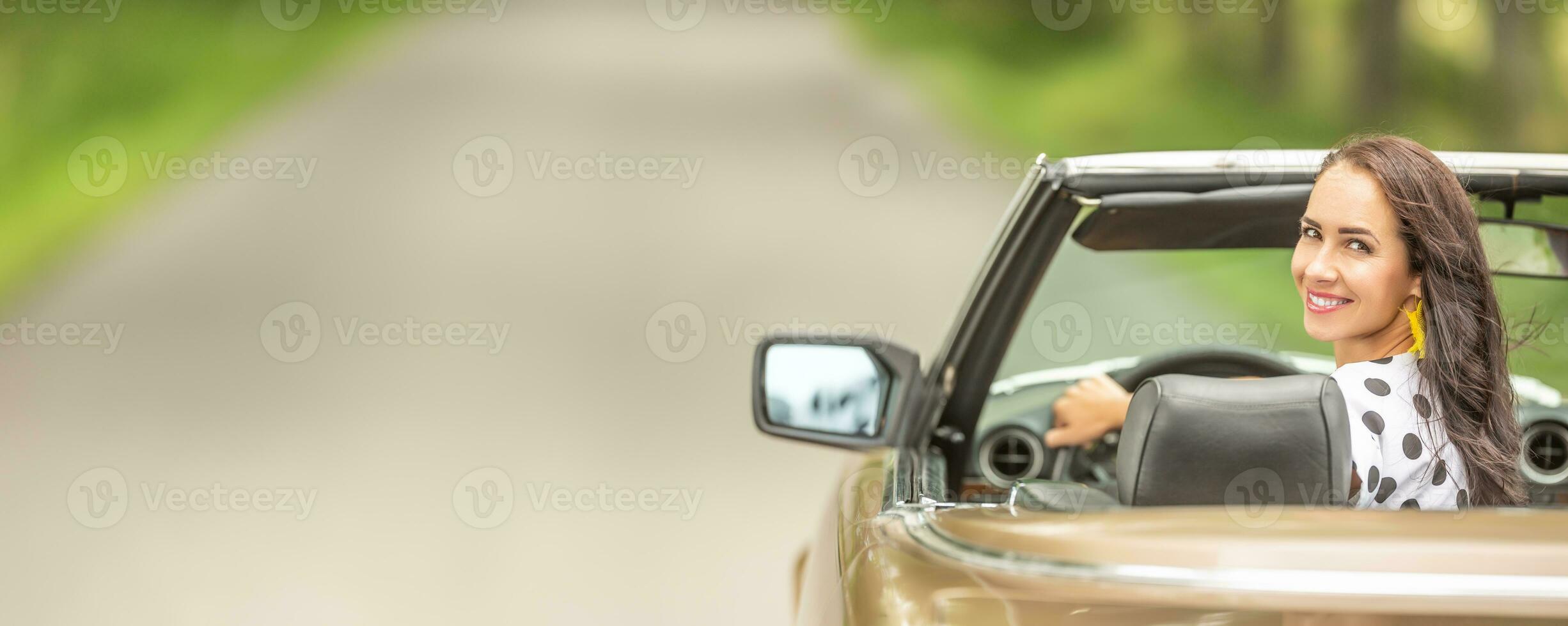 Woman driving in a cabriolet looks back and smiles into the camera. photo