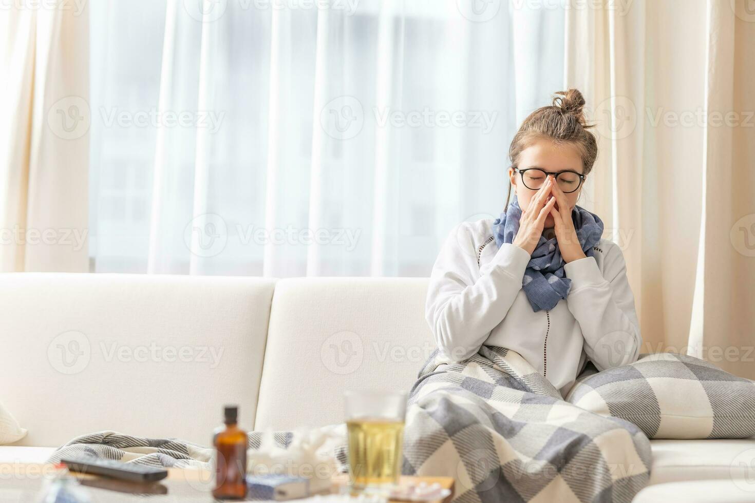 Girl sitting on a sofa and sneezing because of cold and fever photo