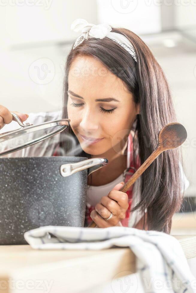 Female with closed eyes smelling freshly cooked food from a cooking pot with a wooden spoon in her hand photo