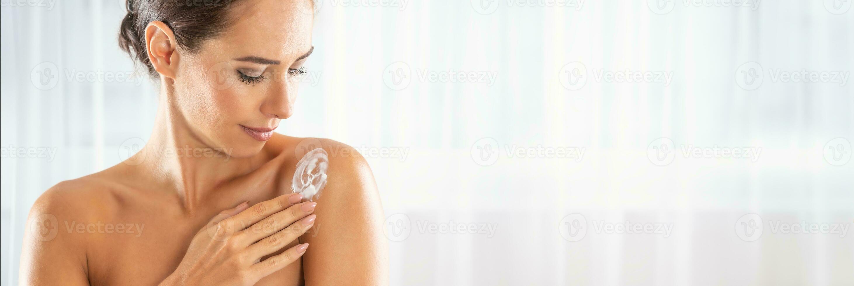 Beautiful young woman applying cream to her shoulder. Skincare spa wellness and cosmetics concept photo